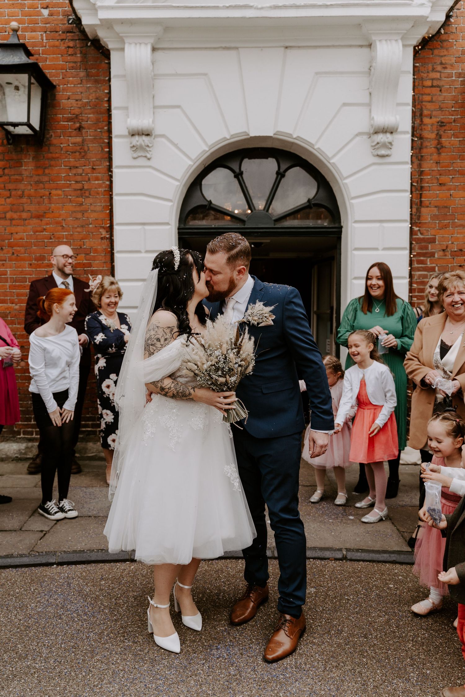 bride and groom kiss as guests throw purple confetti over them.