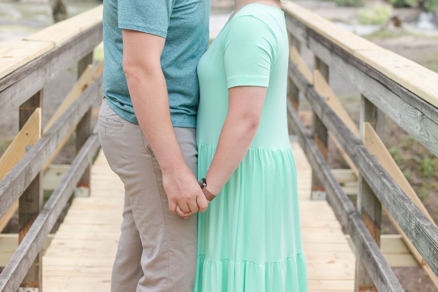 Close-up details of a couple in mint green and gray outfits holding hands on a wooden bridge.