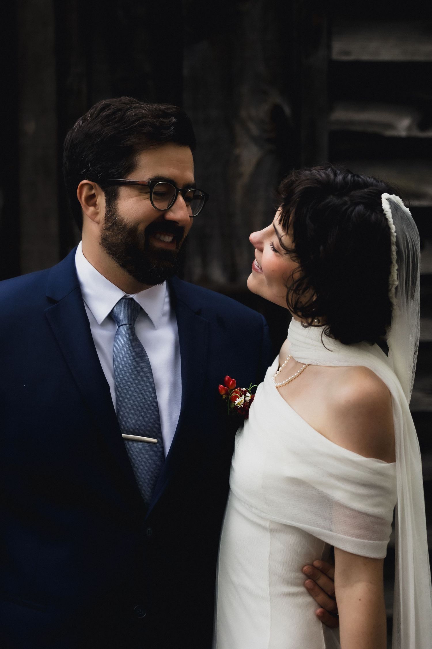 A romantic wedding portrait showing a couple in elegant attire against a dark background.