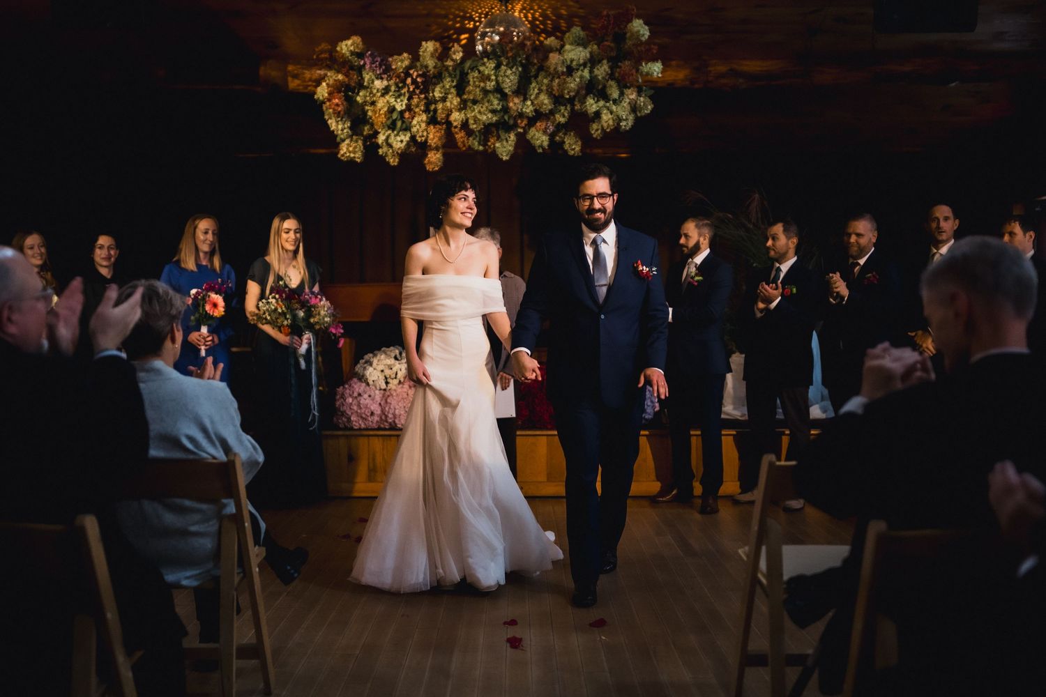 Wedding celebration with couple walking down aisle under warm lights and floral decor.