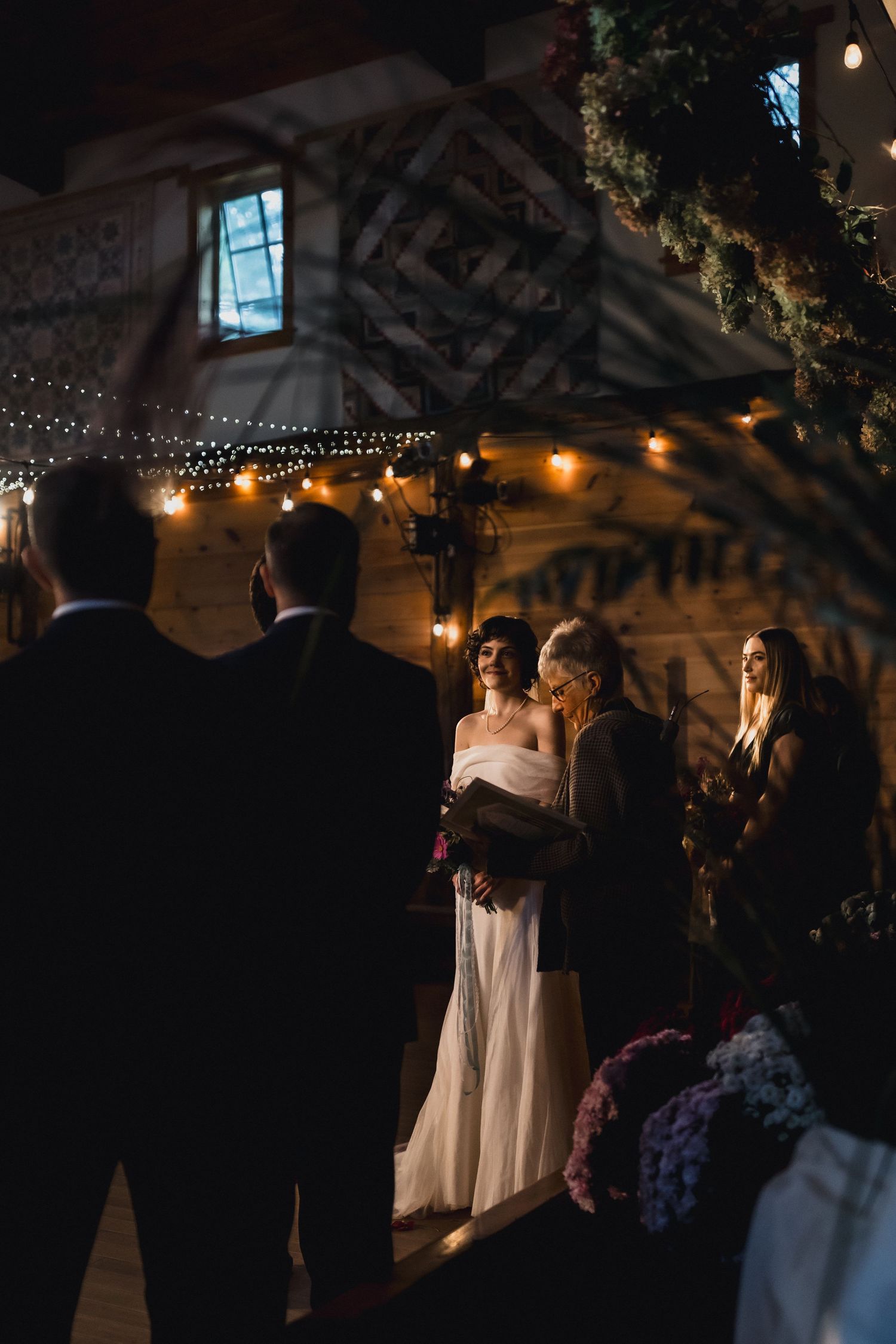 Intimate wedding moment captured in dimly lit rustic venue with string lights and wooden beams.