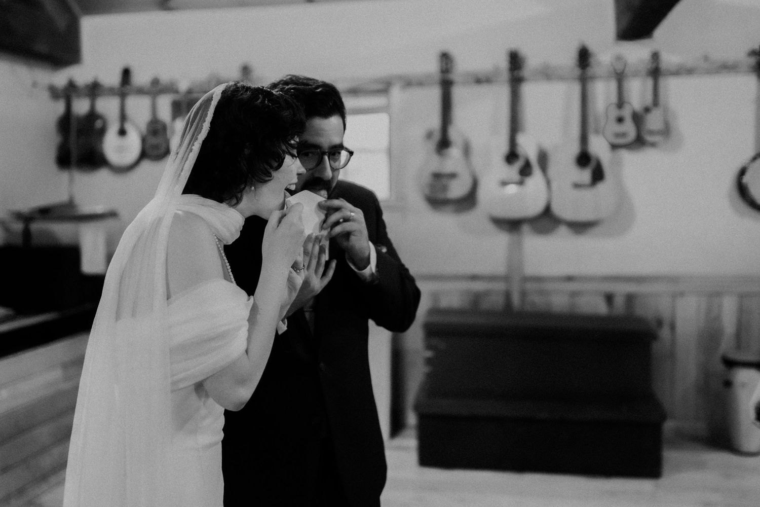 A black and white wedding photo with acoustic guitars displayed on the wall behind the couple.