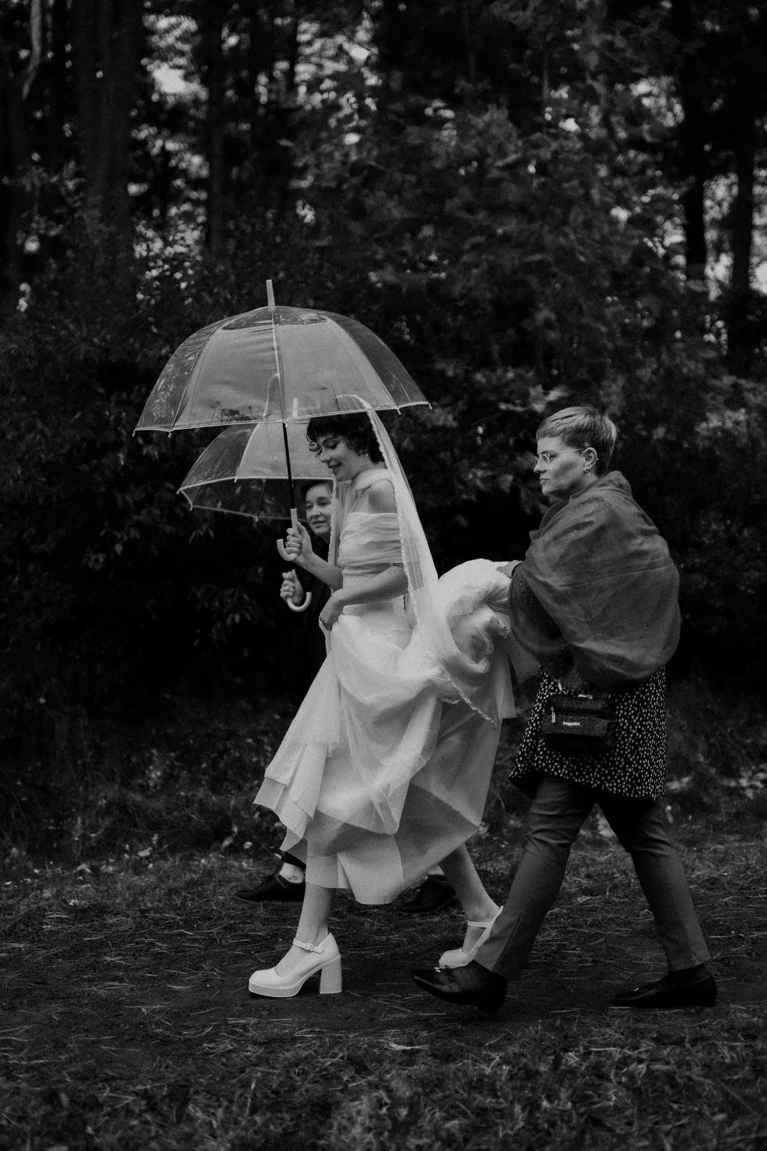 People walking with clear umbrellas in a forest setting during a rainy wedding day.