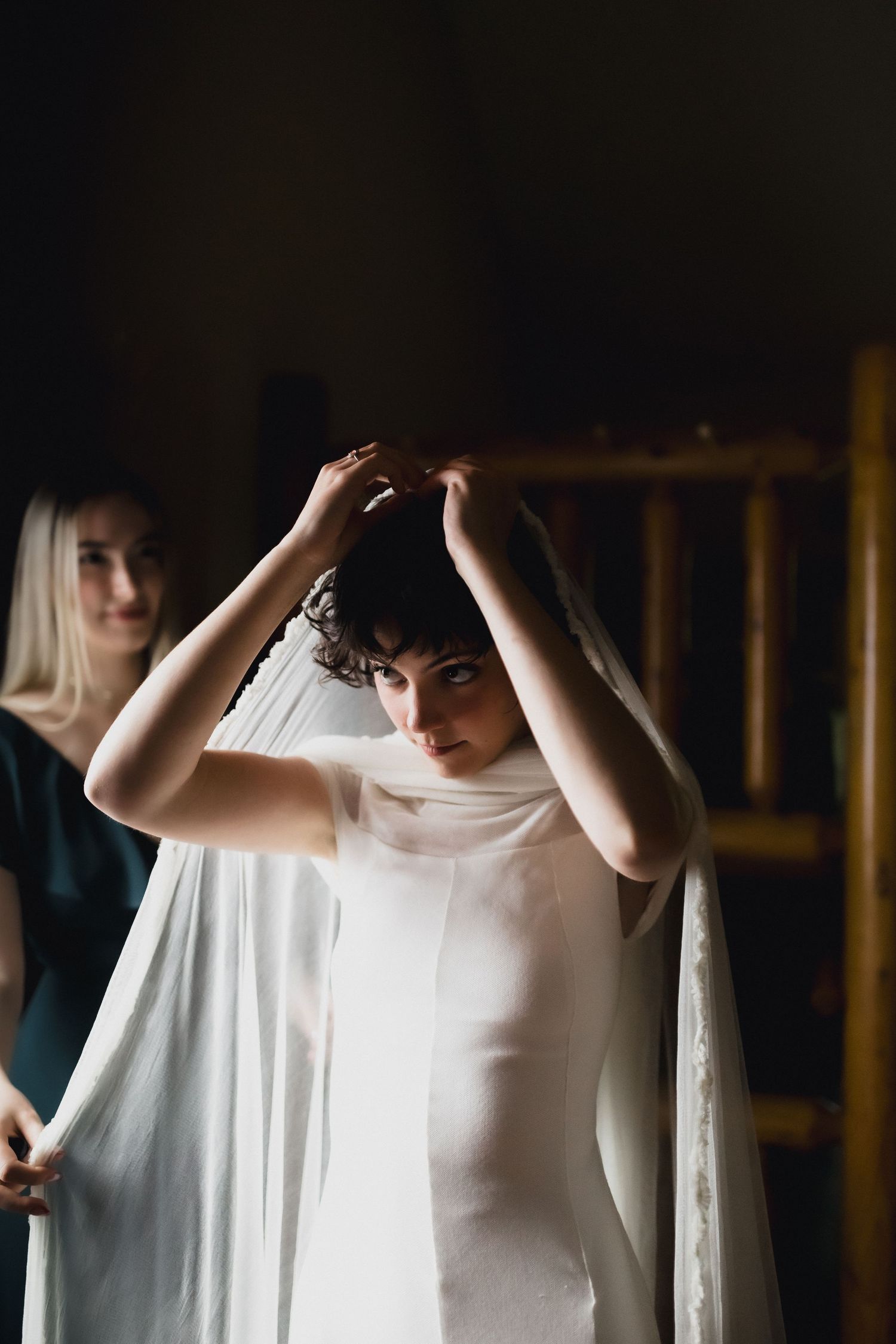 A bride adjusts her veil during wedding preparations in a dimly lit room.
