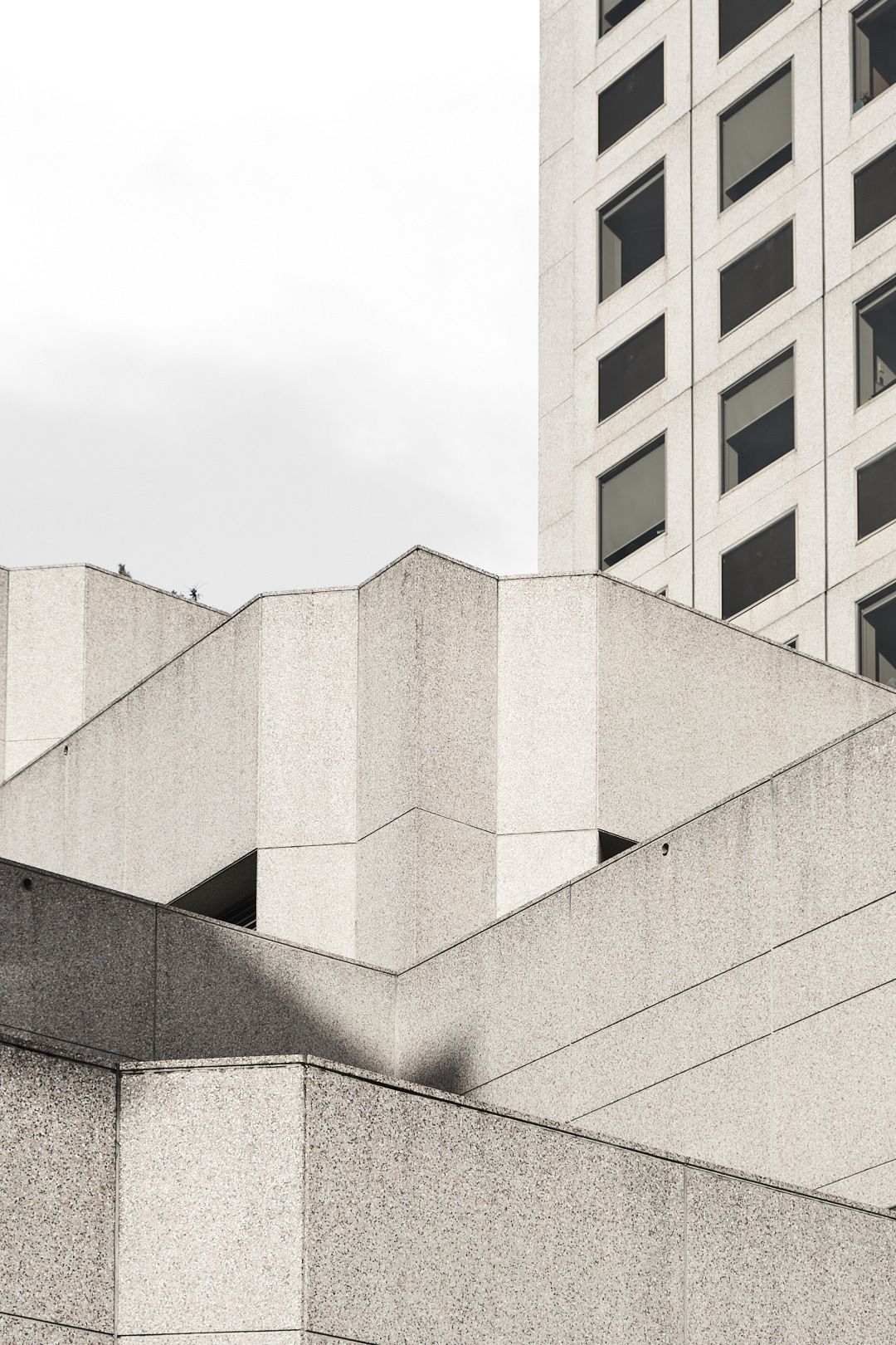 Abstract architectural detail of white modernist building with geometric angles and shadows against cloudy sky.