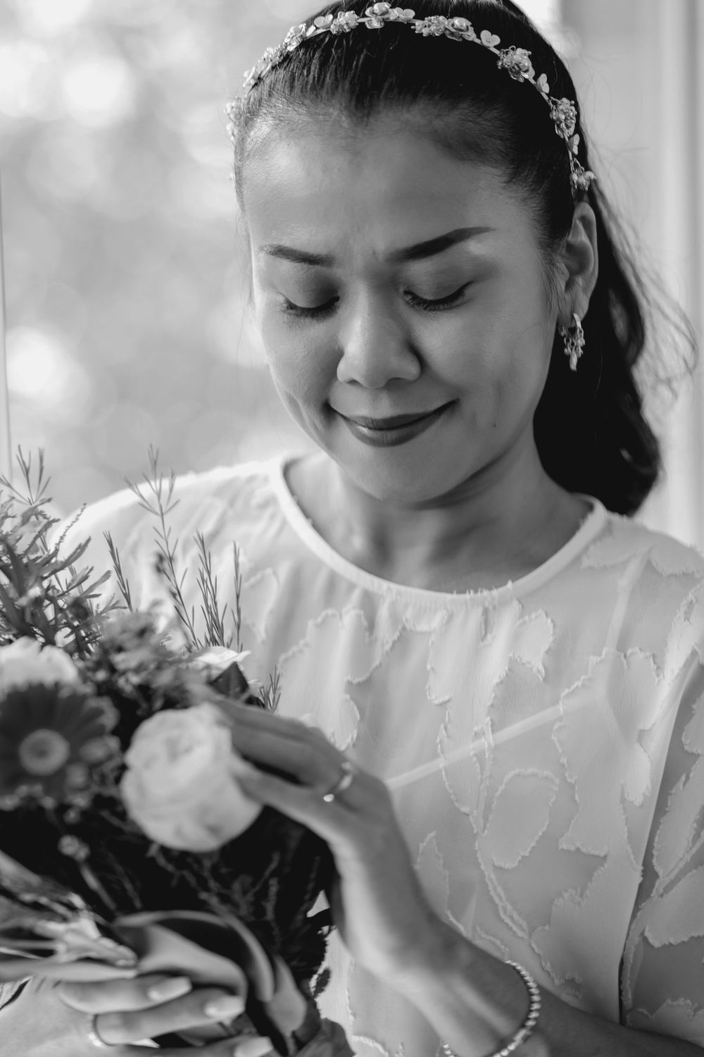 asian bride with slicked back hair and headband holding bouquet and looking at engagement ring