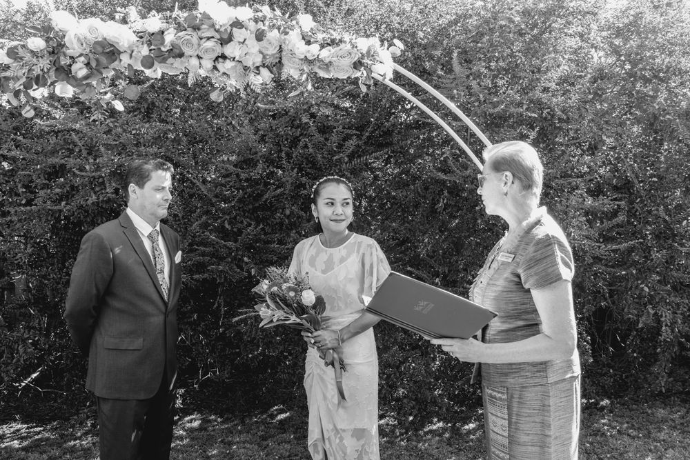 celebrant in skirt suit reading ceremony to mature bride and groom standing under circular arbour