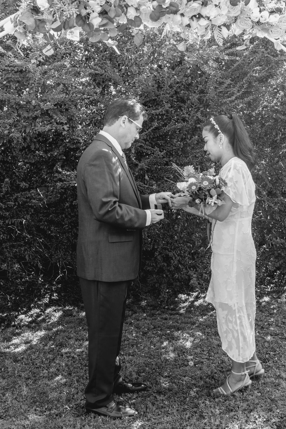 mature groom in suit placing wedding ring on mature asian brides finger