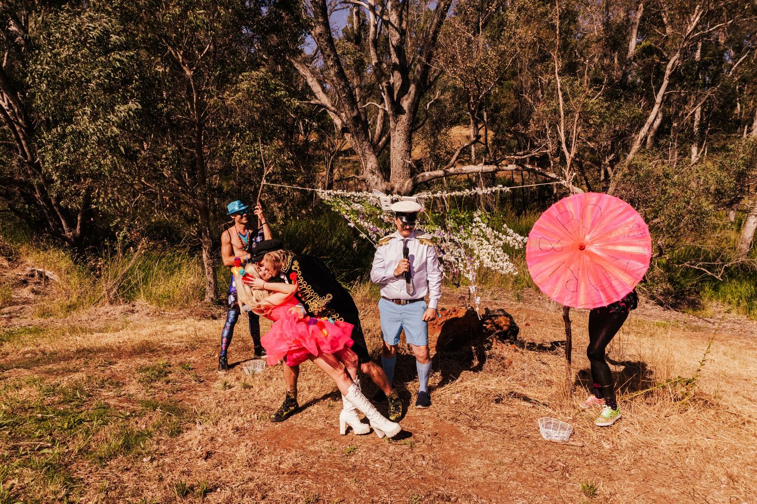 A group poses with a pink umbrella in a rustic outdoor setting.