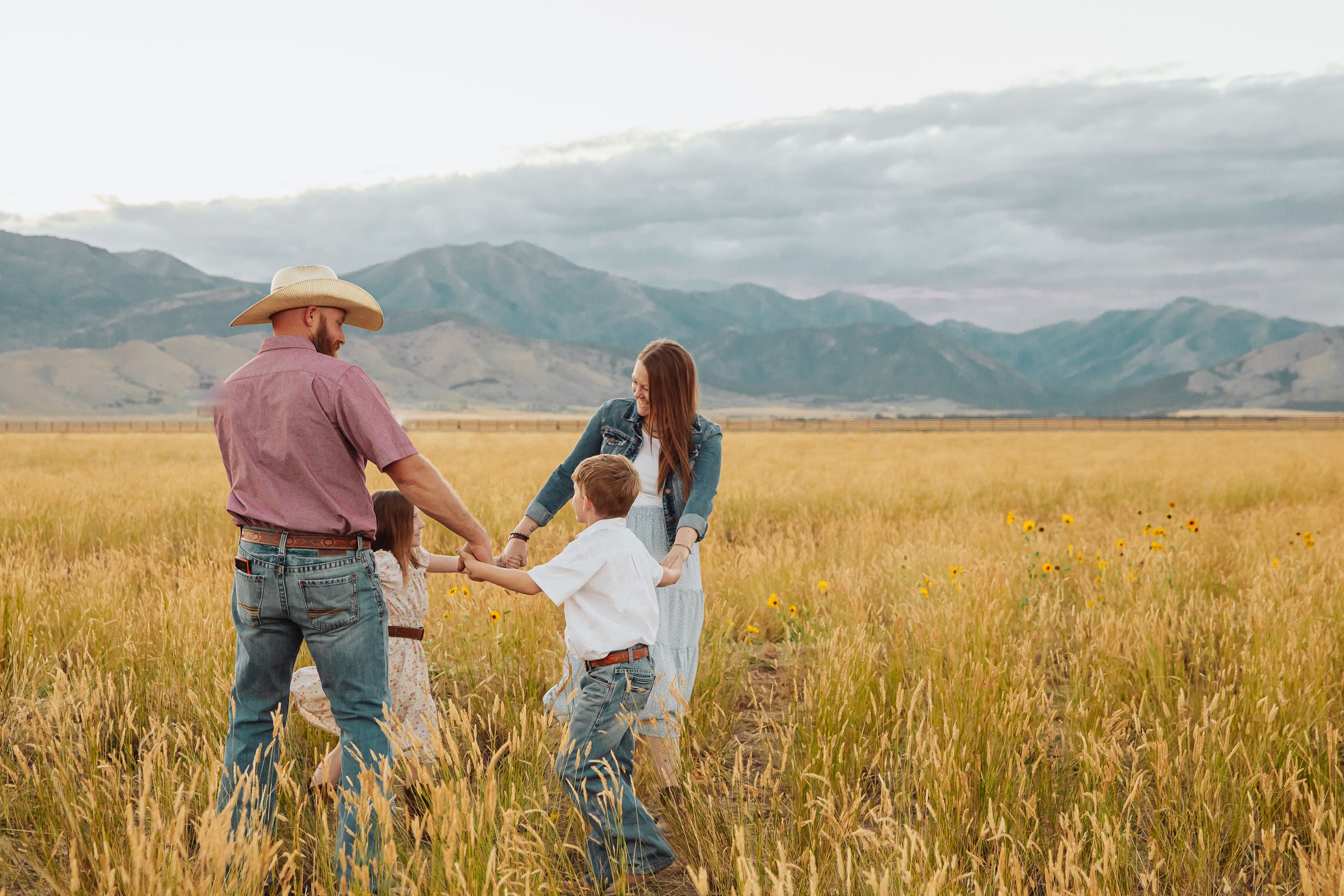 Family playing and running together in a golden wheat field at sunset.
