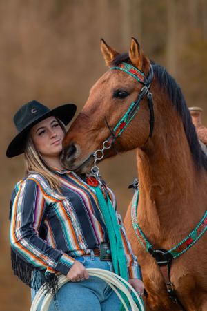 A beautifully groomed chestnut horse with turquoise tack alongside rider in western wear.
