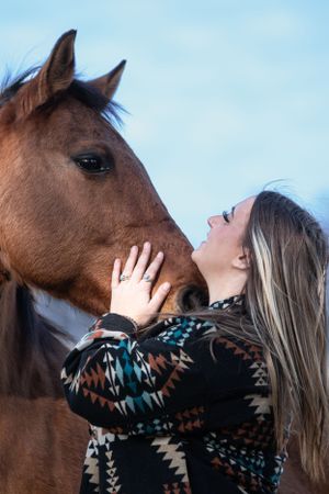 Horse and companion sharing an affectionate moment against blue sky.
