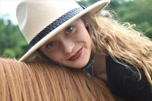 A sunny equestrian portrait featuring a cream colored hat and chestnut horse.