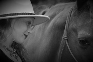 Black and white artistic photograph showing an intimate moment between a person in a western hat and a horse.