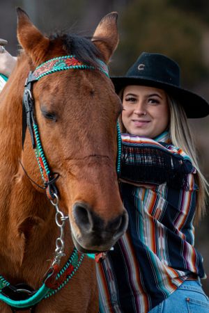 Close-up of a brown horse wearing turquoise tack and western riding gear in an outdoor setting.