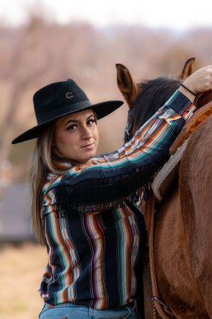 Close-up shot of a horse and rider in southwestern attire with striped shirt and black hat.