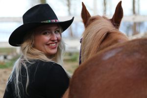 Western style portrait with black cowboy hat against a rustic barn background.