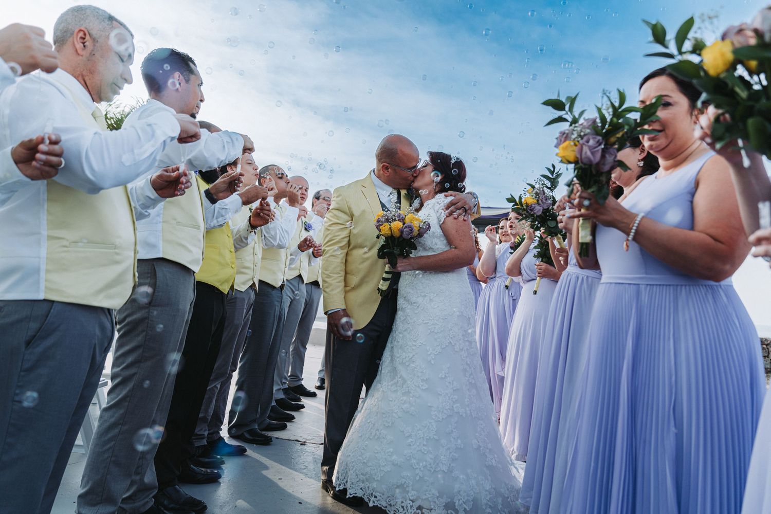 Wedding party in lavender dresses and yellow shirts during outdoor ceremony.