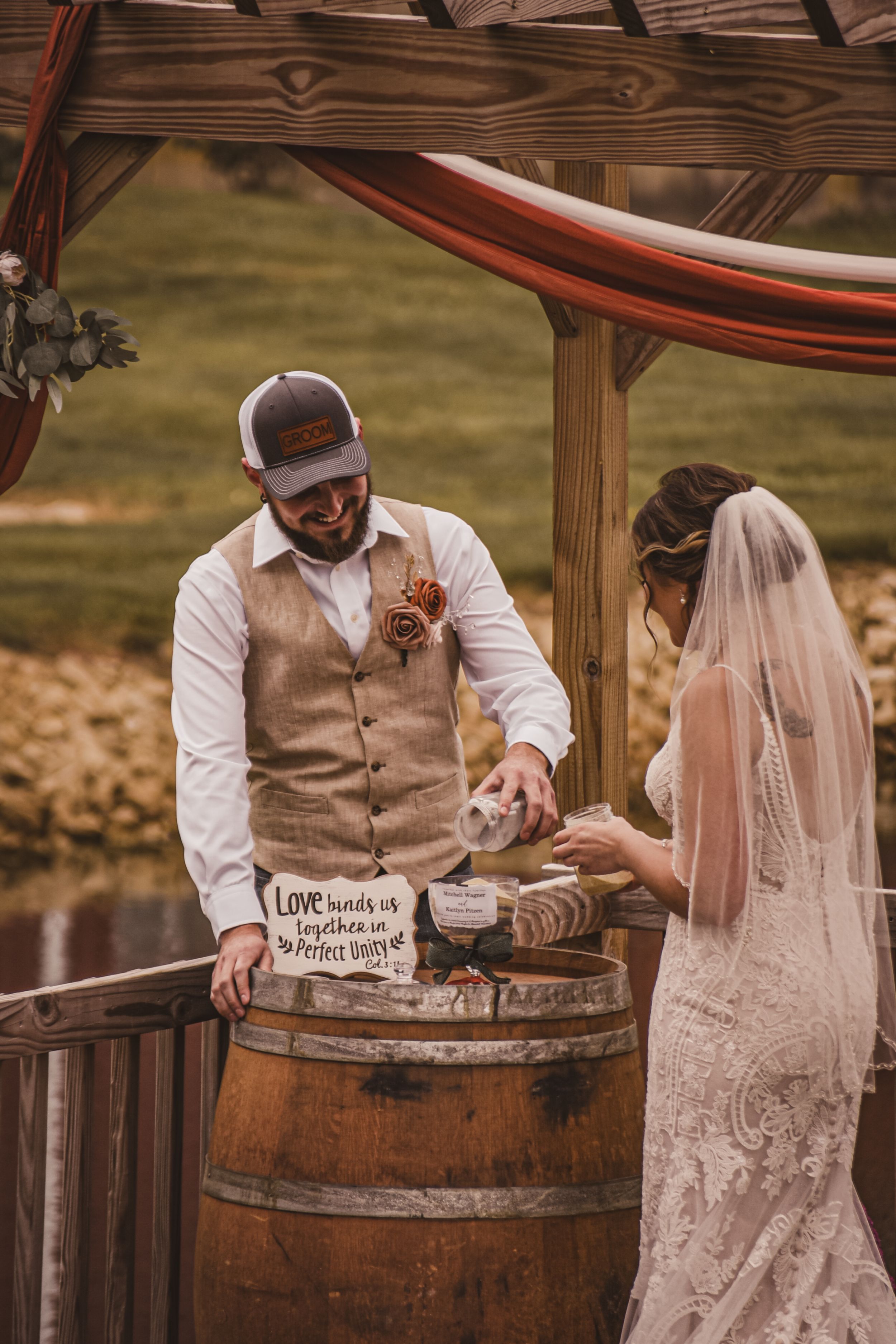 Wedding ceremony featuring couple pouring ingredients into mason jars on wooden barrel.