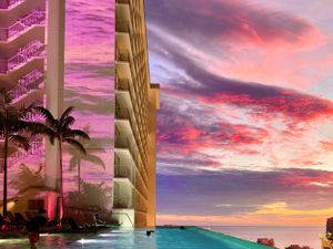 Luxury resort infinity pool overlooking ocean at sunset with pink and purple sky and palm trees. Realestate Photography