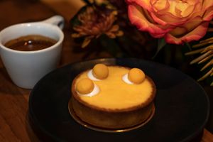 Orange-yellow tart with small round decorations served alongside coffee and roses. Food Photography