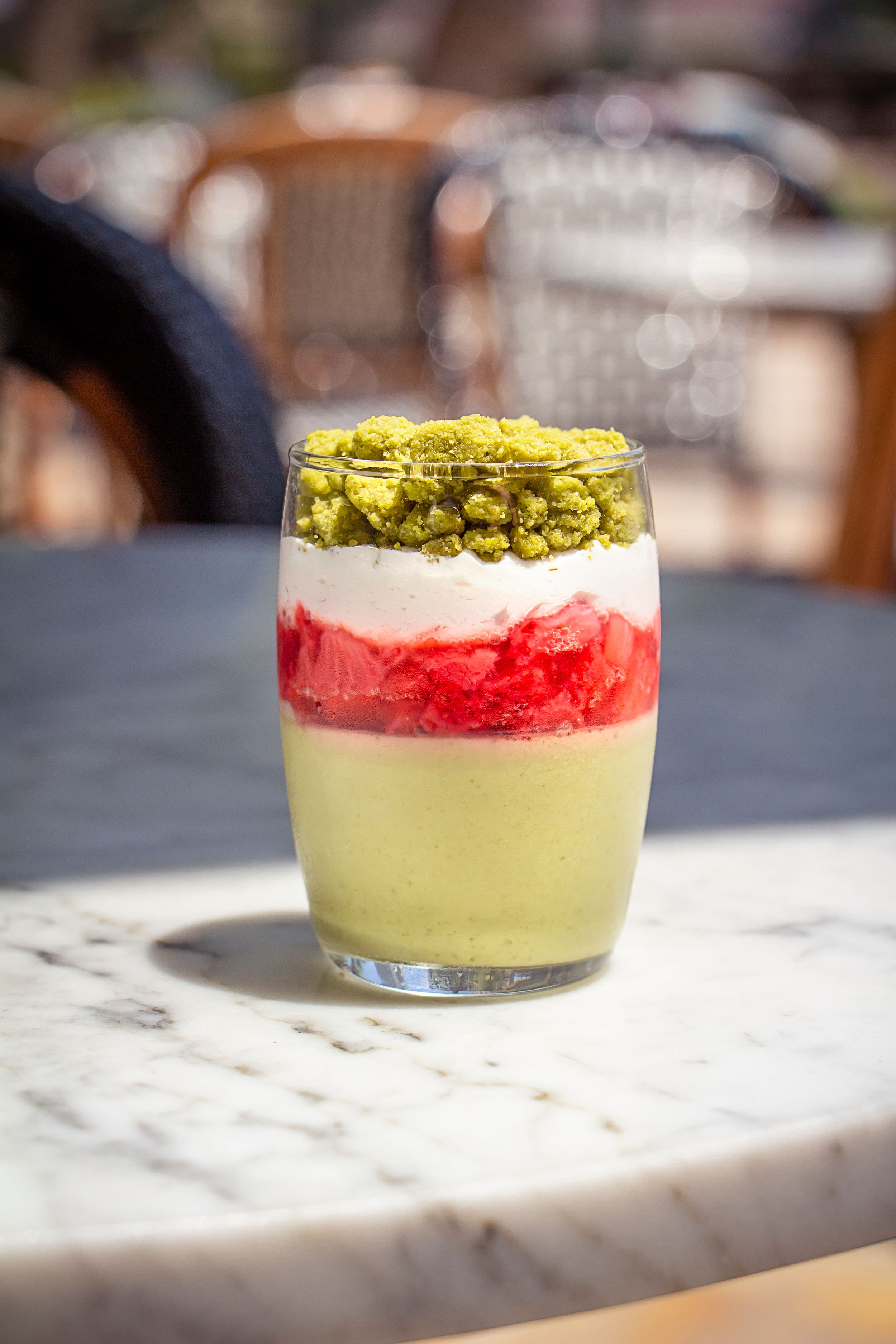 Layered dessert glass with pistachio, cream and red fruit components on marble table. Product photography
