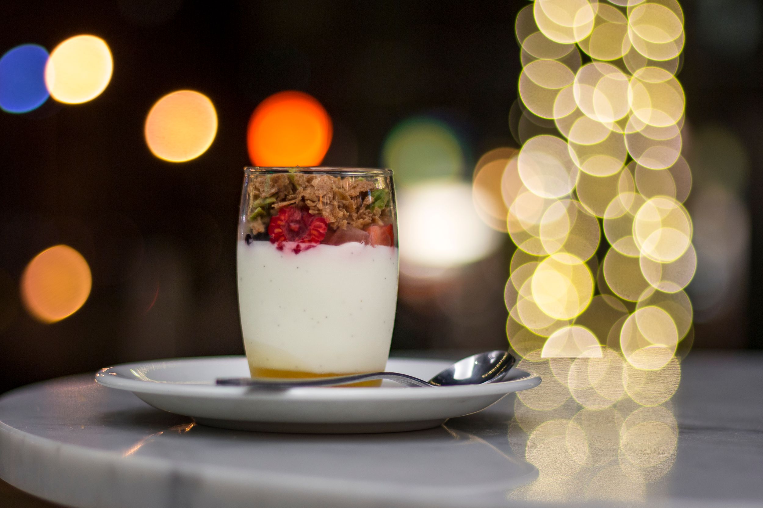 A dessert glass filled with cream and berries against blurred bokeh lights. Product Photography