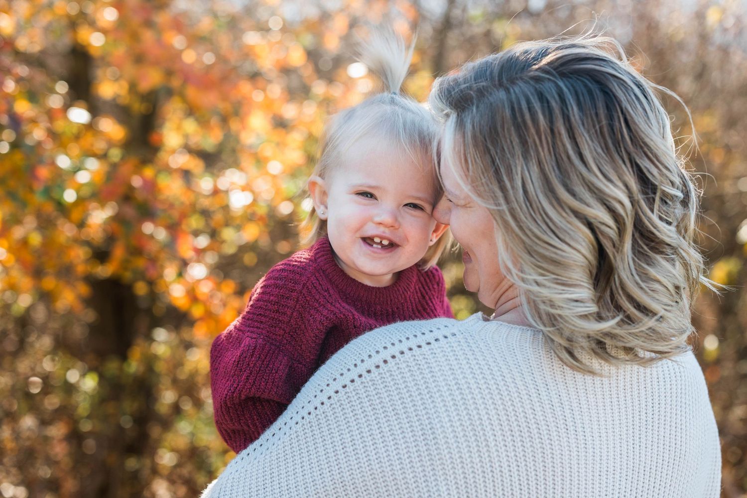 A joyful autumn portrait of mother and baby sharing a tender moment against colorful fall foliage.