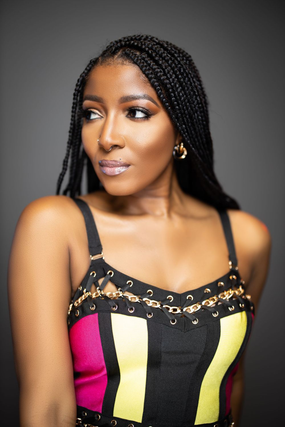 Fashion portrait highlighting braided hair and colorful striped corset top against grey backdrop.