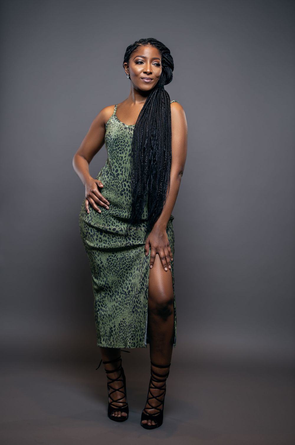 Full-length fashion photo in green sequined dress with strappy black heels against grey background.