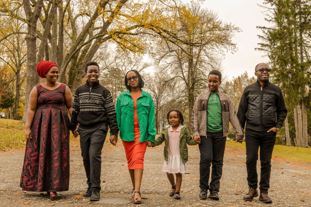 A diverse family of six walks together on an autumn path wearing coordinated casual outfits.