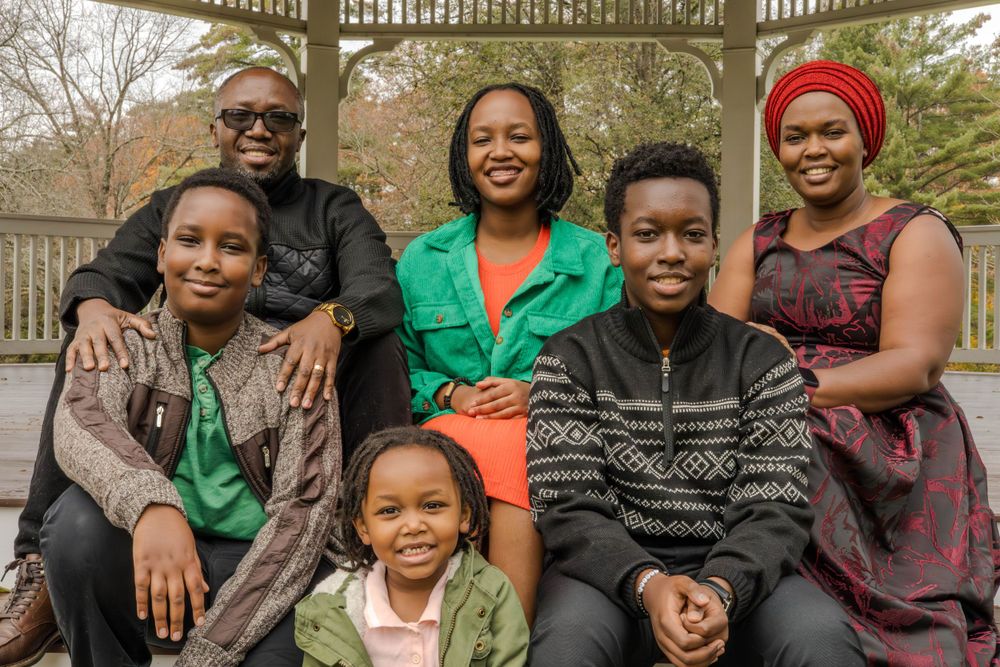 A happy family poses together on wooden bench outdoors during fall season.