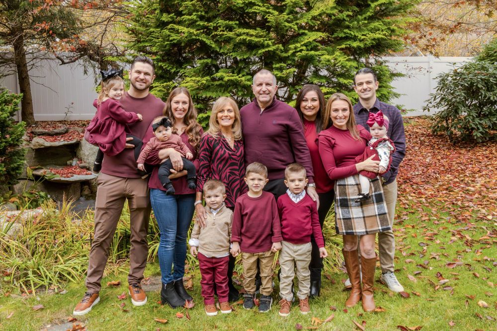 Large family group in coordinating burgundy outfits poses together for outdoor autumn portrait.
