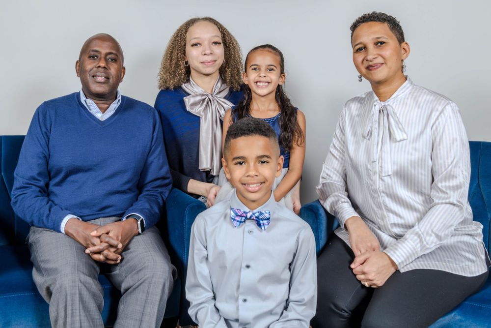 Multi-generational family poses formally on blue couch for indoor portrait.