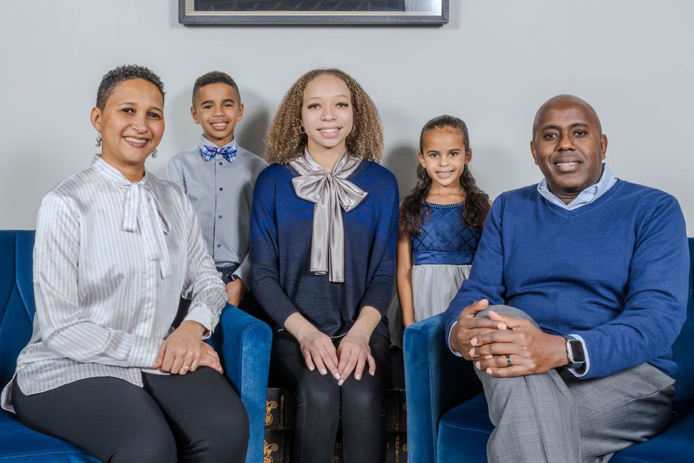 Family of five poses together on blue couch wearing coordinated formal attire.