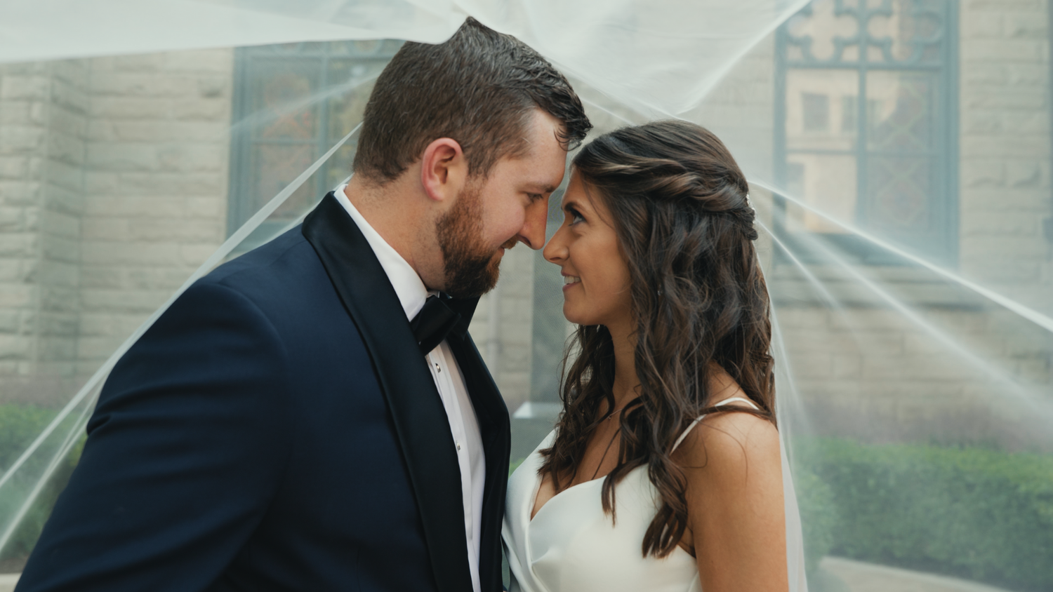 Romantic wedding couple sharing intimate moment under glass canopy.