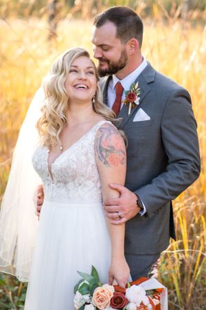 Joyful wedding portrait in golden wheat field with autumn-themed bouquet.