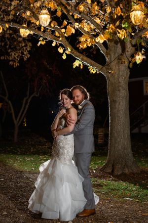 Romantic nighttime wedding portrait under tree decorated with glowing lanterns.