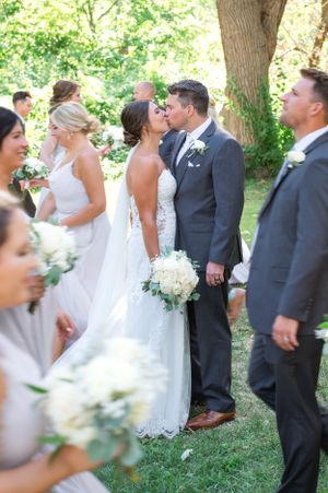 Garden wedding ceremony moment surrounded by greenery and white floral bouquets.