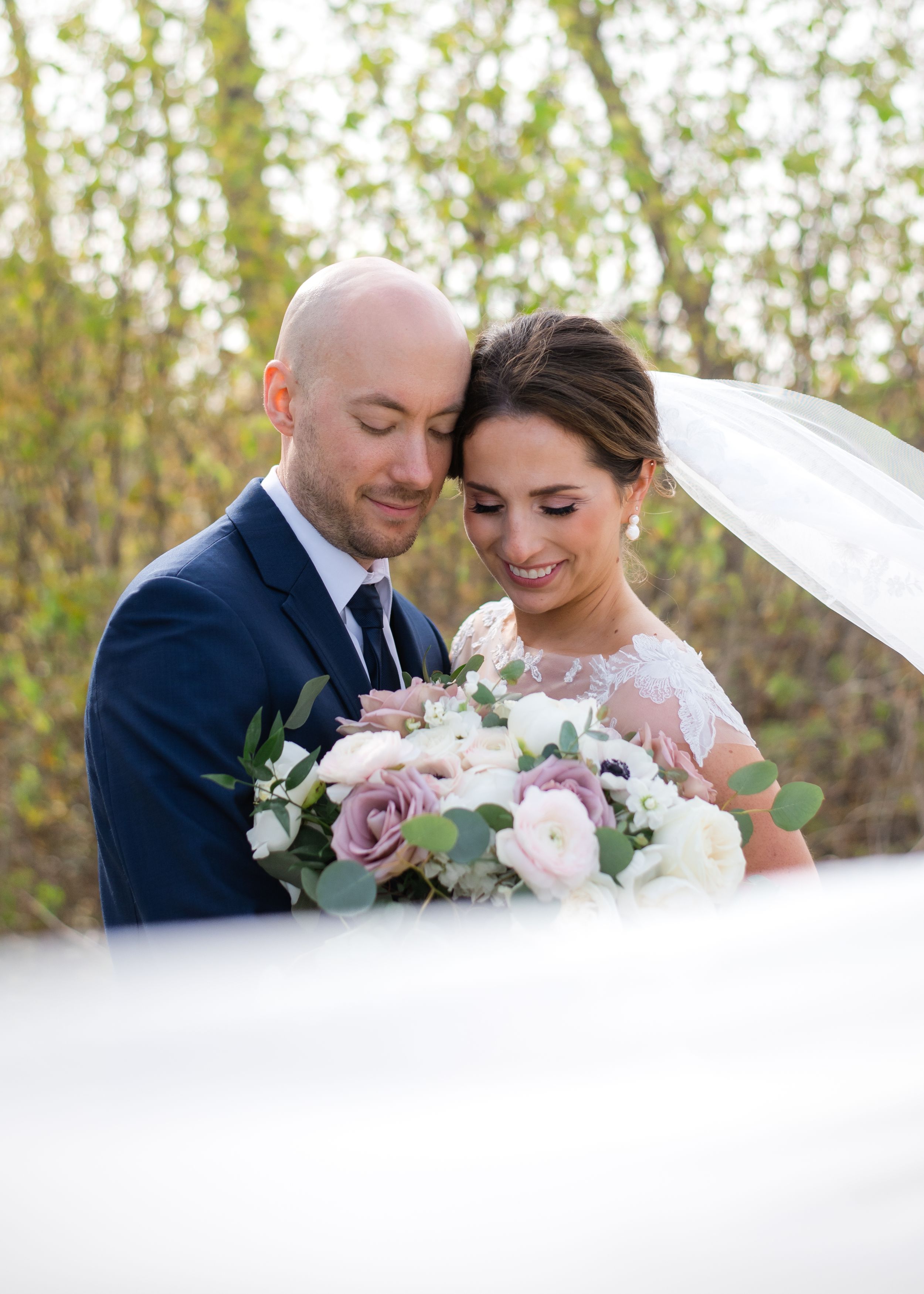 Elegant wedding portrait with delicate pink and purple bouquet against natural backdrop.