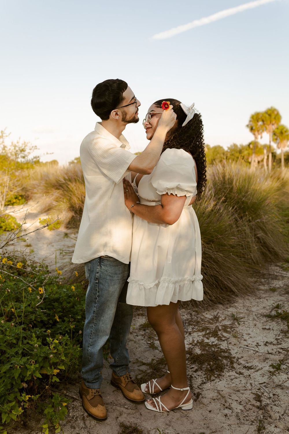 a romantic picture of a guy putting a rose on his fiance's ear