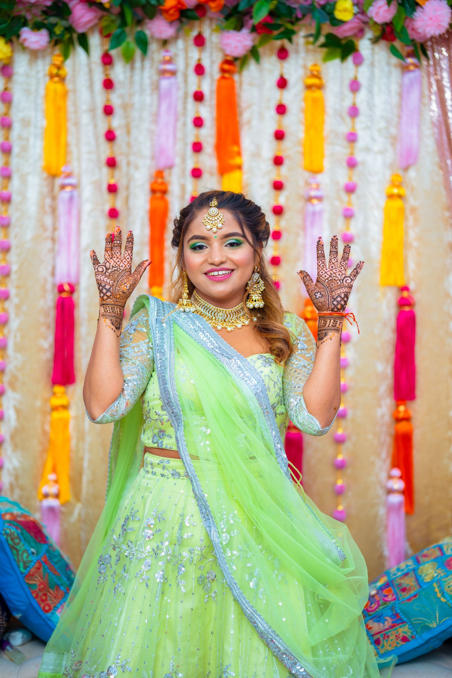 Traditional Indian outfit in mint green with decorative henna designs on hands against vibrant backdrop.