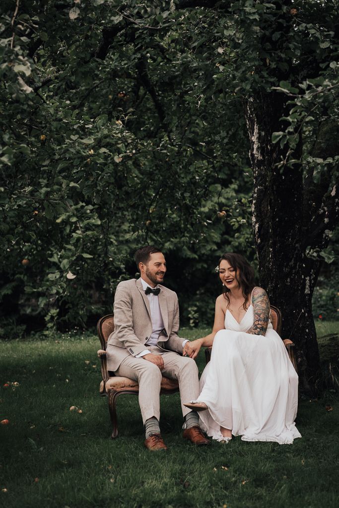 Brudpar sitter under sitt äppelträd och skrattar. Bröllopsfotografering i Eskilstuna.