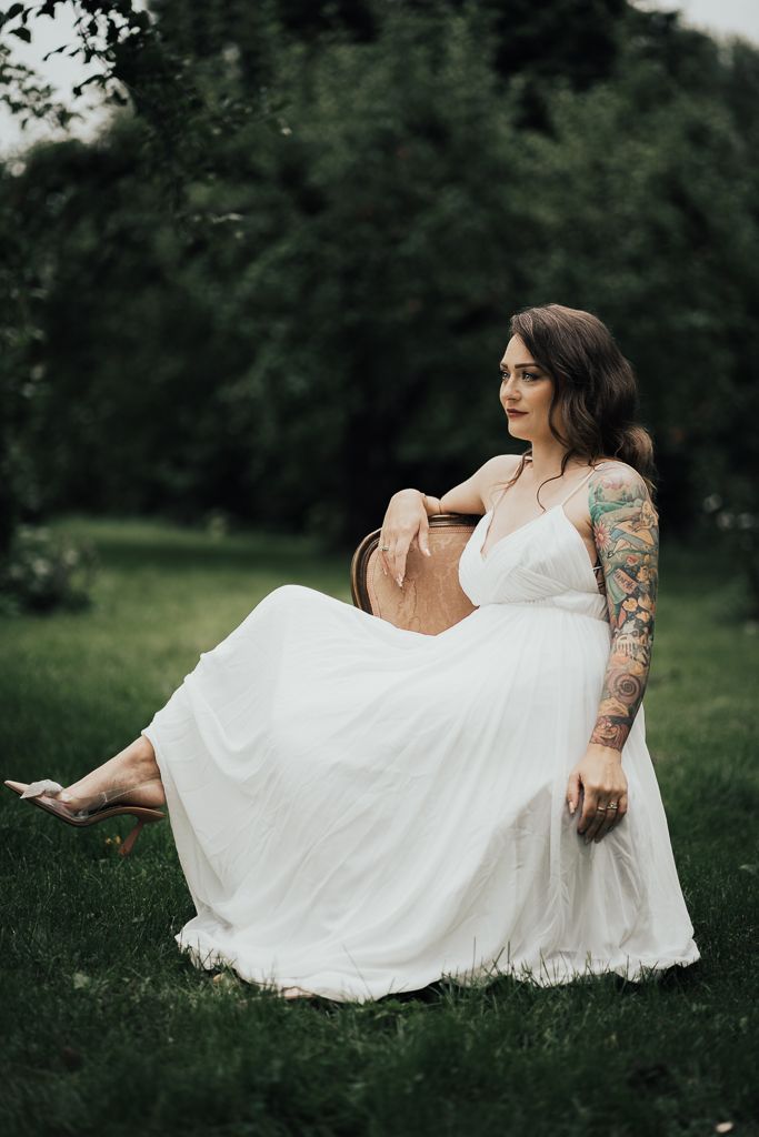 Brud sitter på vintagestol i sin trädgård. Bröllopsfotografering i Eskilstuna.