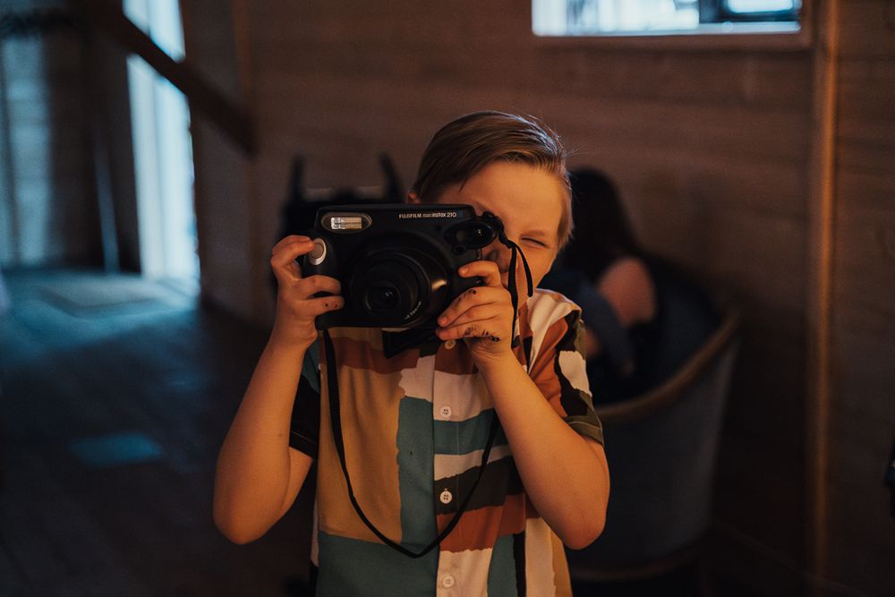 Pojke tar kort på fotografen med en polaroidkamera. Bröllopsfotografering på Vindsmagasinet i Eskilstuna.