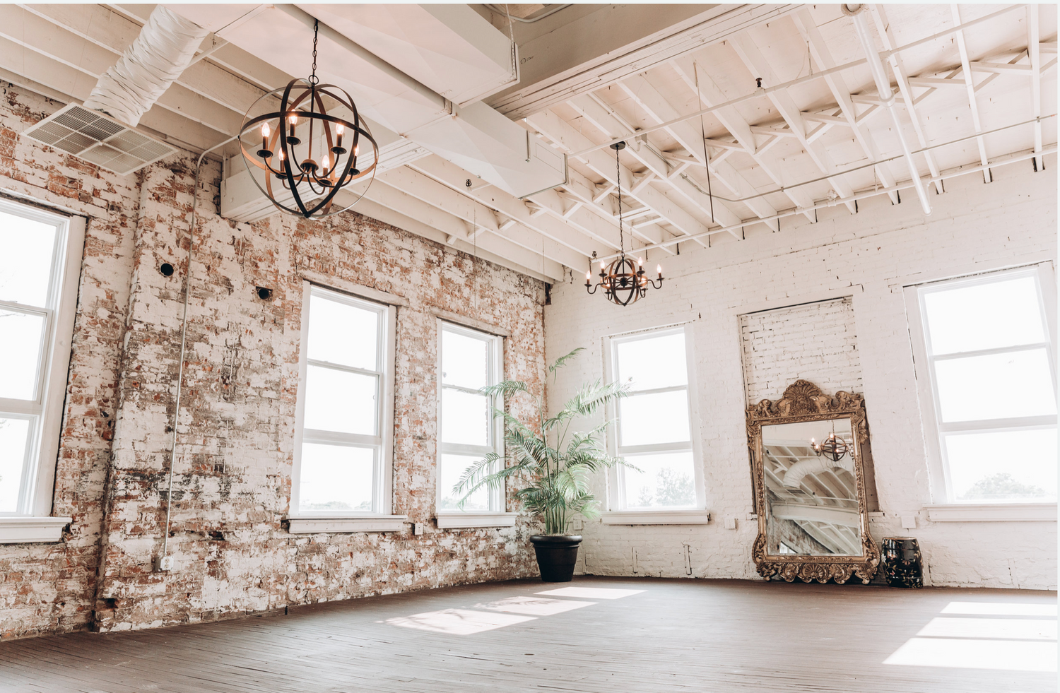 Industrial style white loft interior with exposed ceiling beams and brick walls illuminated by natural light.
