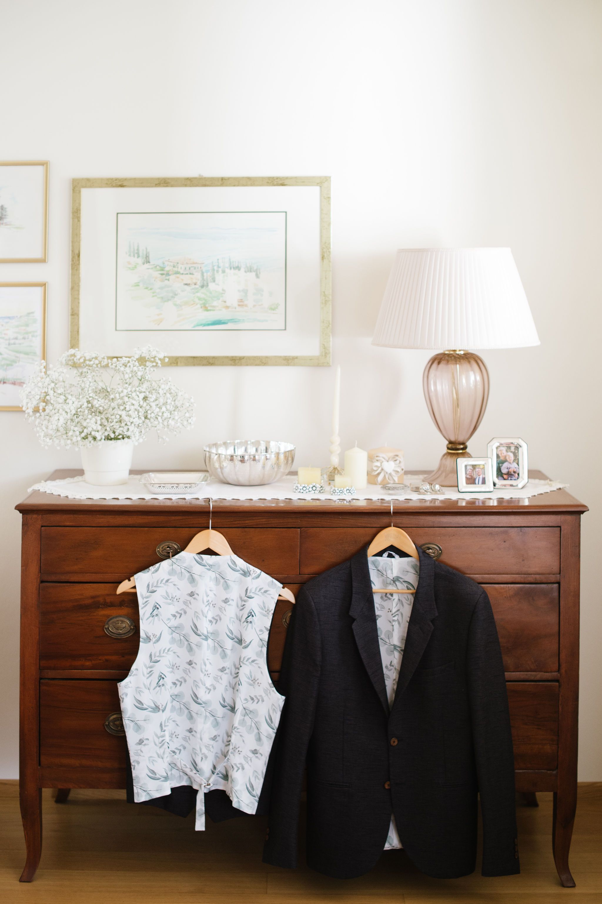Wedding attire displayed on vintage dresser with lamp and framed artwork.