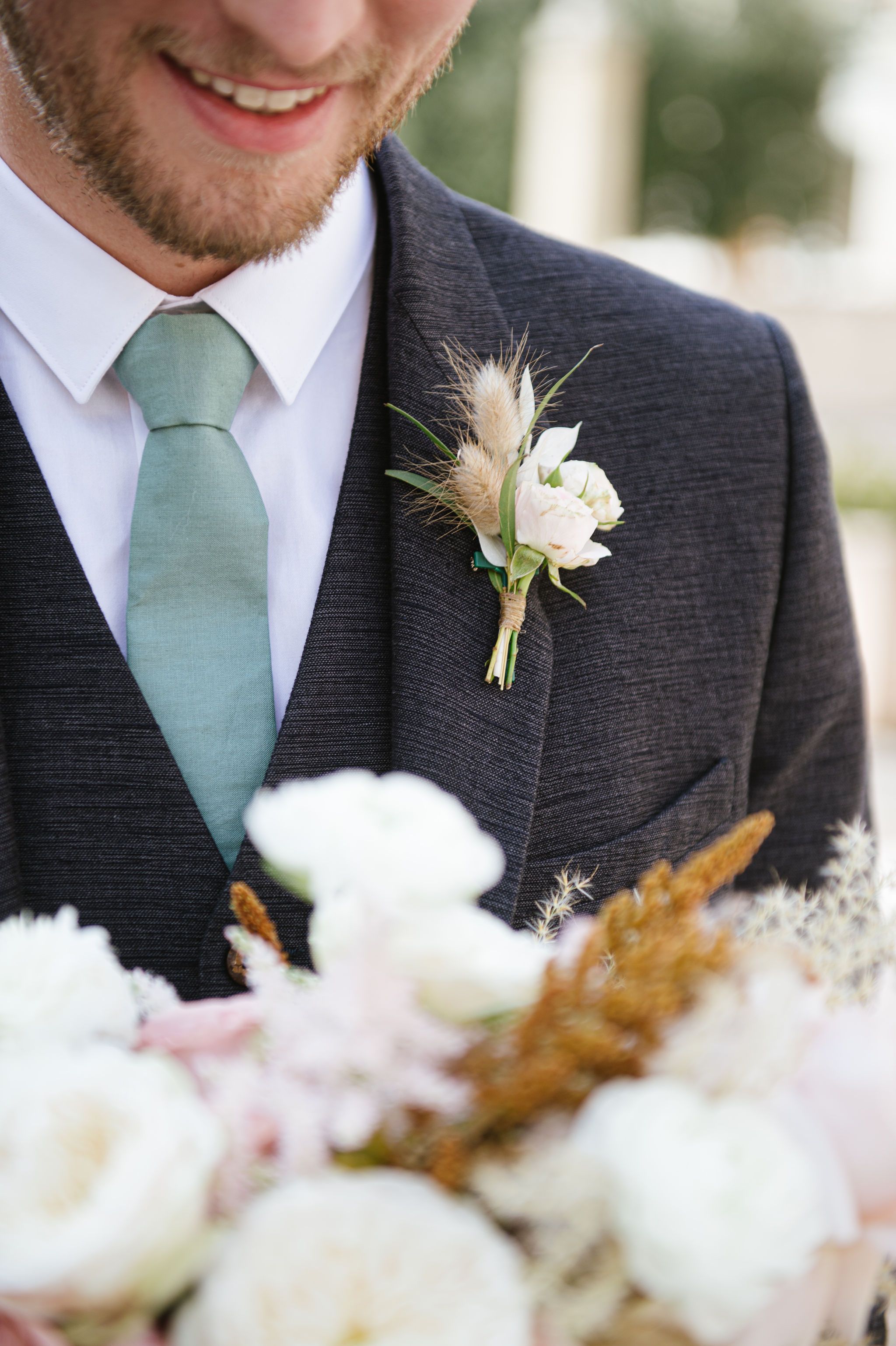 Close-up of groom's boutonniere with white rose and mint green tie.