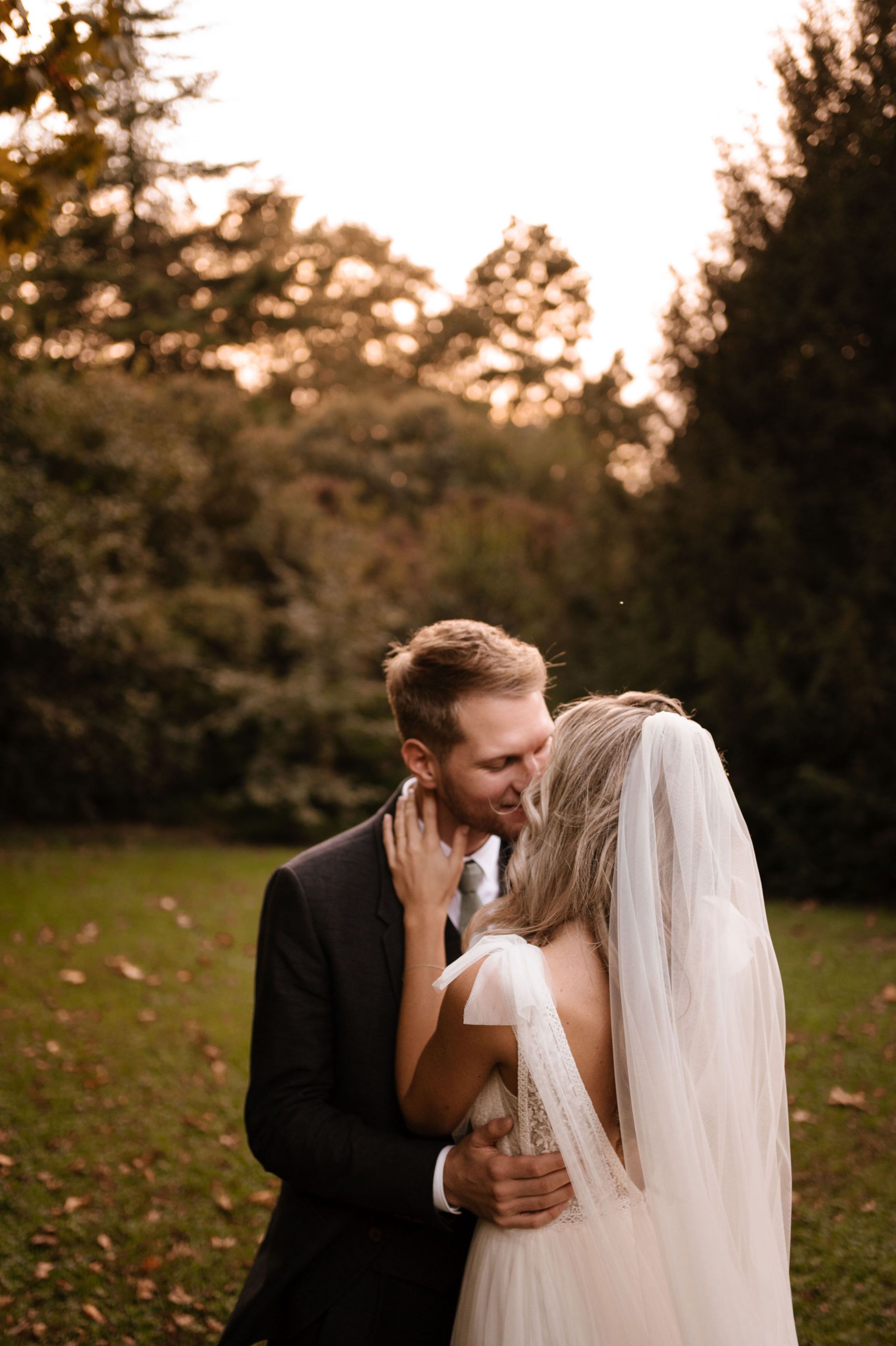 Romantic sunset wedding photo of newlyweds embracing in a garden with golden light filtering through trees.