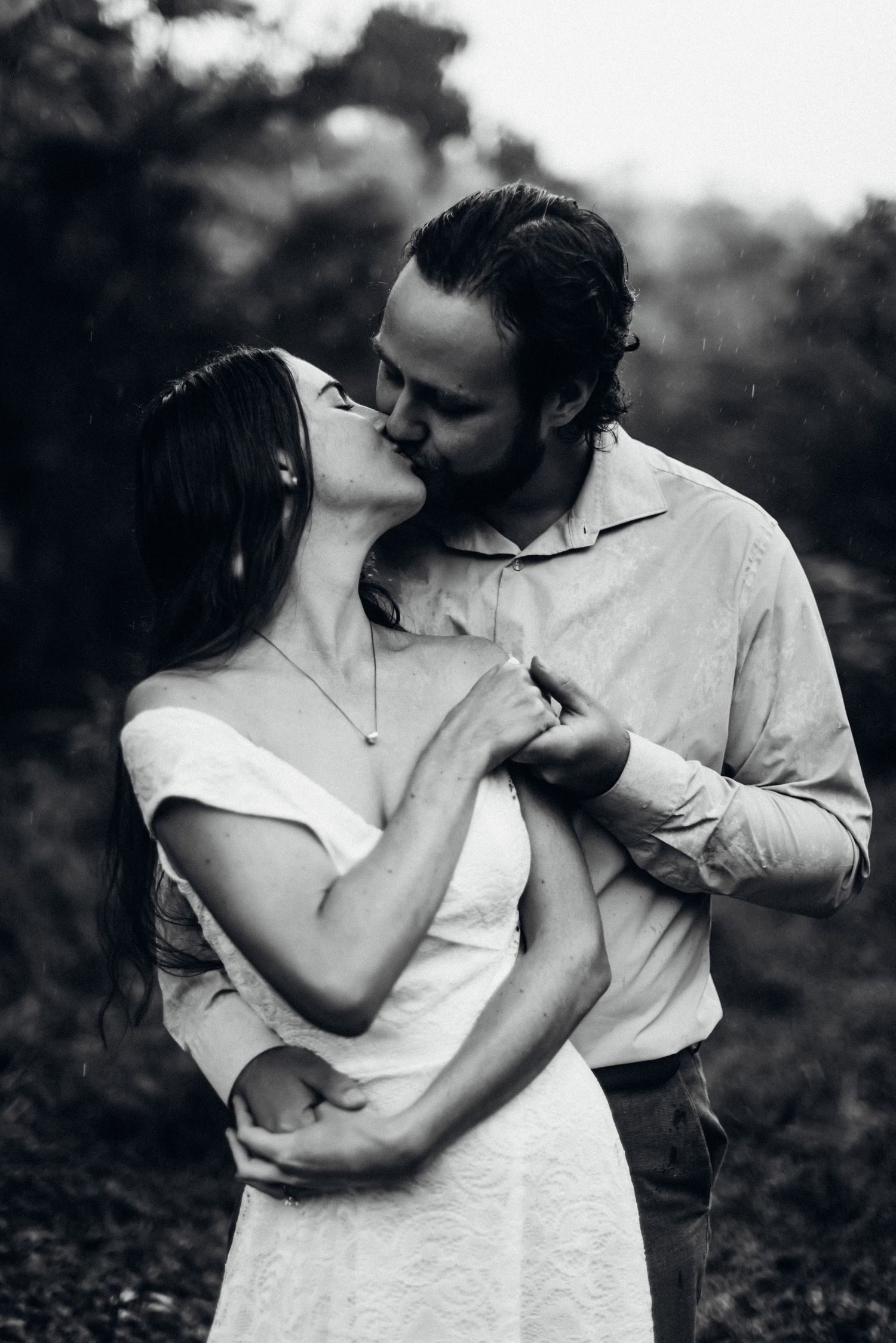 A romantic black and white photo of a couple sharing an intimate kiss outdoors.